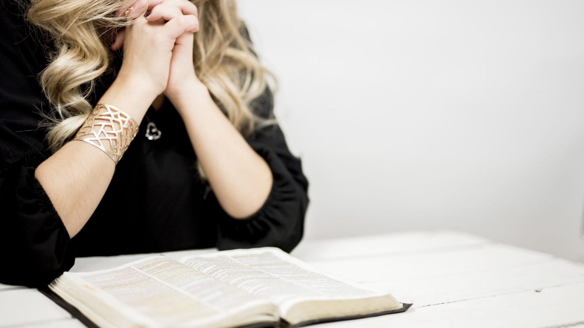 A selective closeup shot of a female praying with tightly linked fingers near an open book on a table